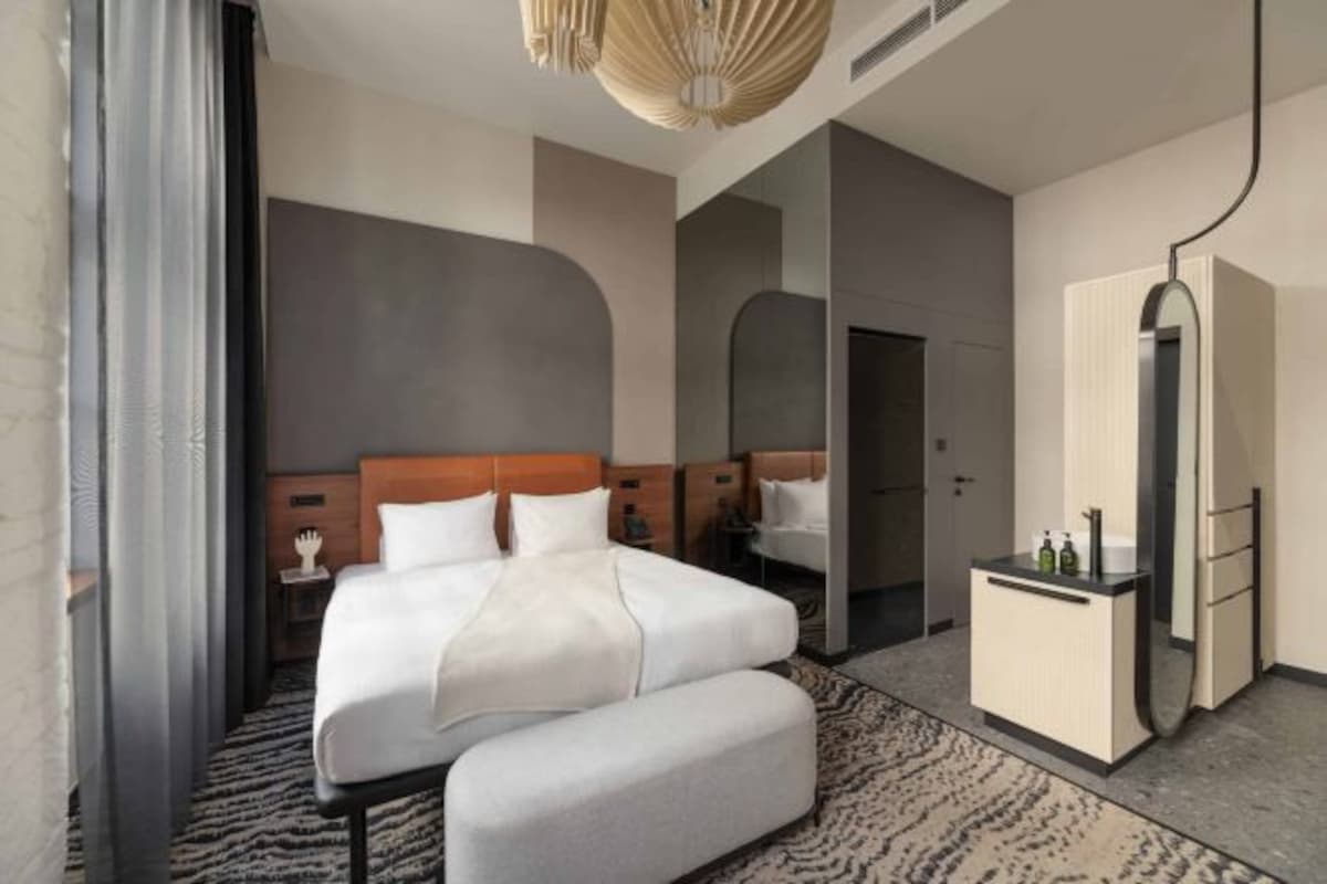 Una habitación de hotel moderna con una cama grande, una mesita de noche, un armario y un espejo.
