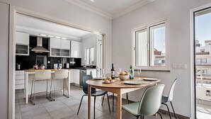 Een moderne keuken met witte kasten, een eetgedeelte met een houten tafel en stoelen, en uitzicht op de stad door grote ramen.