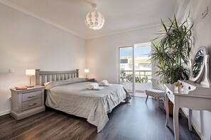 Et soveværelse med seng, natborde, skrivebord med spejl, en potteplante og en balkon med udsigt.