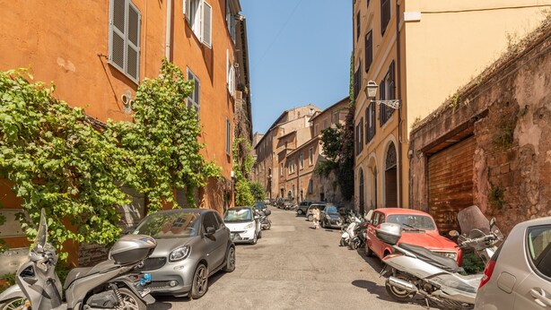 A narrow street lined with parked cars and motorcycles, buildings with shutters, and a clear blue sky. - Monti Charming Design Apartment (Roma)
