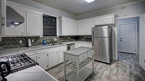 A modern kitchen with white cabinets, stainless steel appliances, and a glass island. - Walk to Downtown Fondren | King Beds (Jackson)