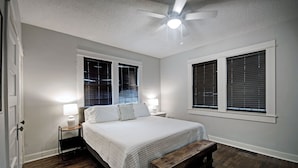 A bedroom with a bed, two bedside tables, a nightstand, a ceiling fan, and two windows with blinds. - Walk to Downtown Fondren | King Beds (Jackson)