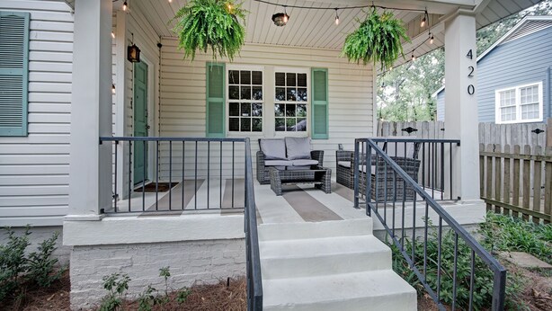 A porch with a set of stairs leading up to a seating area, a wooden fence, and a hanging plant. - Walk to Downtown Fondren | King Beds (Jackson)