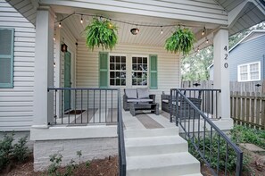 A porch with a set of stairs leading up to a seating area, a wooden fence, and a hanging plant. - Walk to Downtown Fondren | King Beds (Jackson)