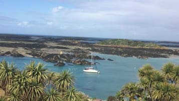 Une vue sur la côte, avec un bateau sur l’eau, des palmiers et des sièges installés à l’extérieur.