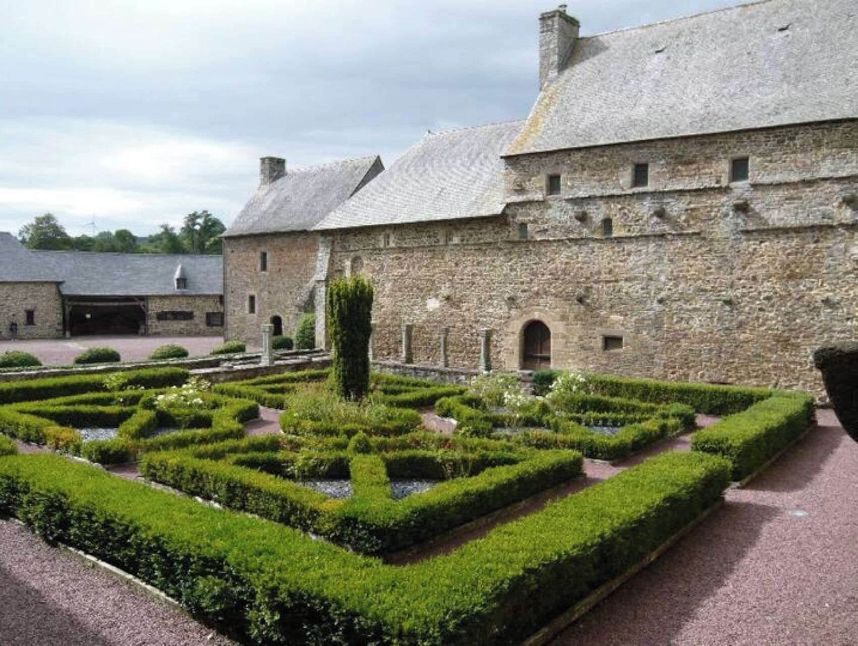 Un bâtiment en pierre avec un jardin à la française devant.