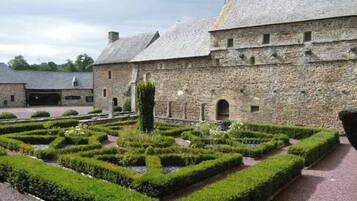 Un bâtiment en pierre avec un jardin à la française devant.