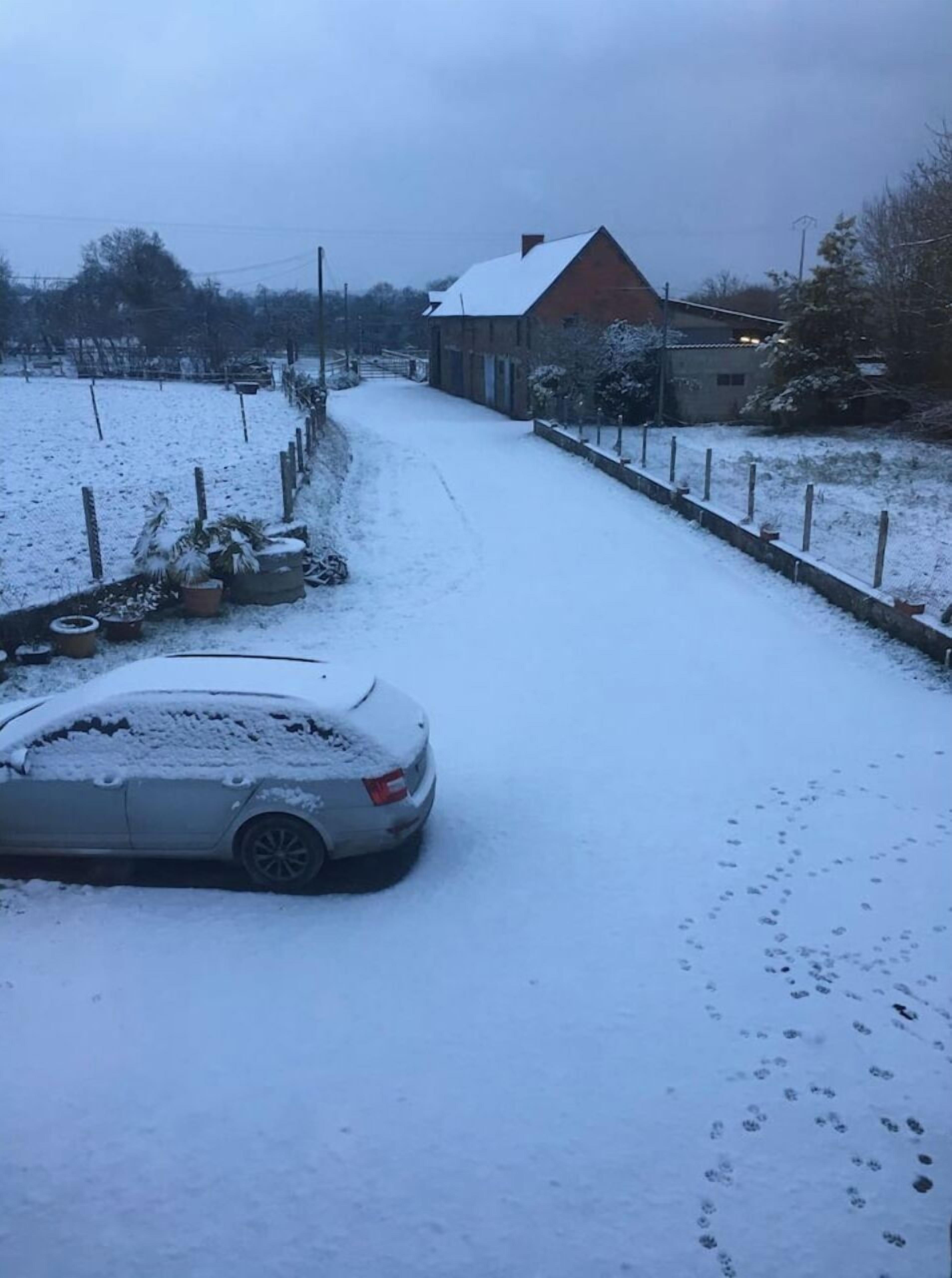 A snow-covered residential street with a parked car and houses.