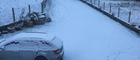 A snow-covered residential street with a parked car and houses.