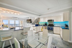 Cozinha moderna com mesa de jantar de vidro, armários brancos e painel de parede azul.