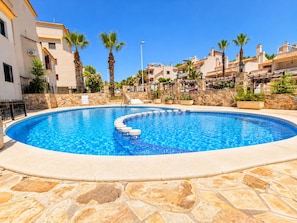 Une piscine bordée de pierres, entourée de bâtiments dotés de balcons et de palmiers.