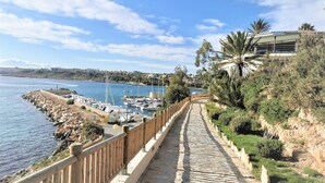 Une promenade en bord de mer avec un sentier en pierre, une rambarde en bois et une vue sur la mer et les bateaux.