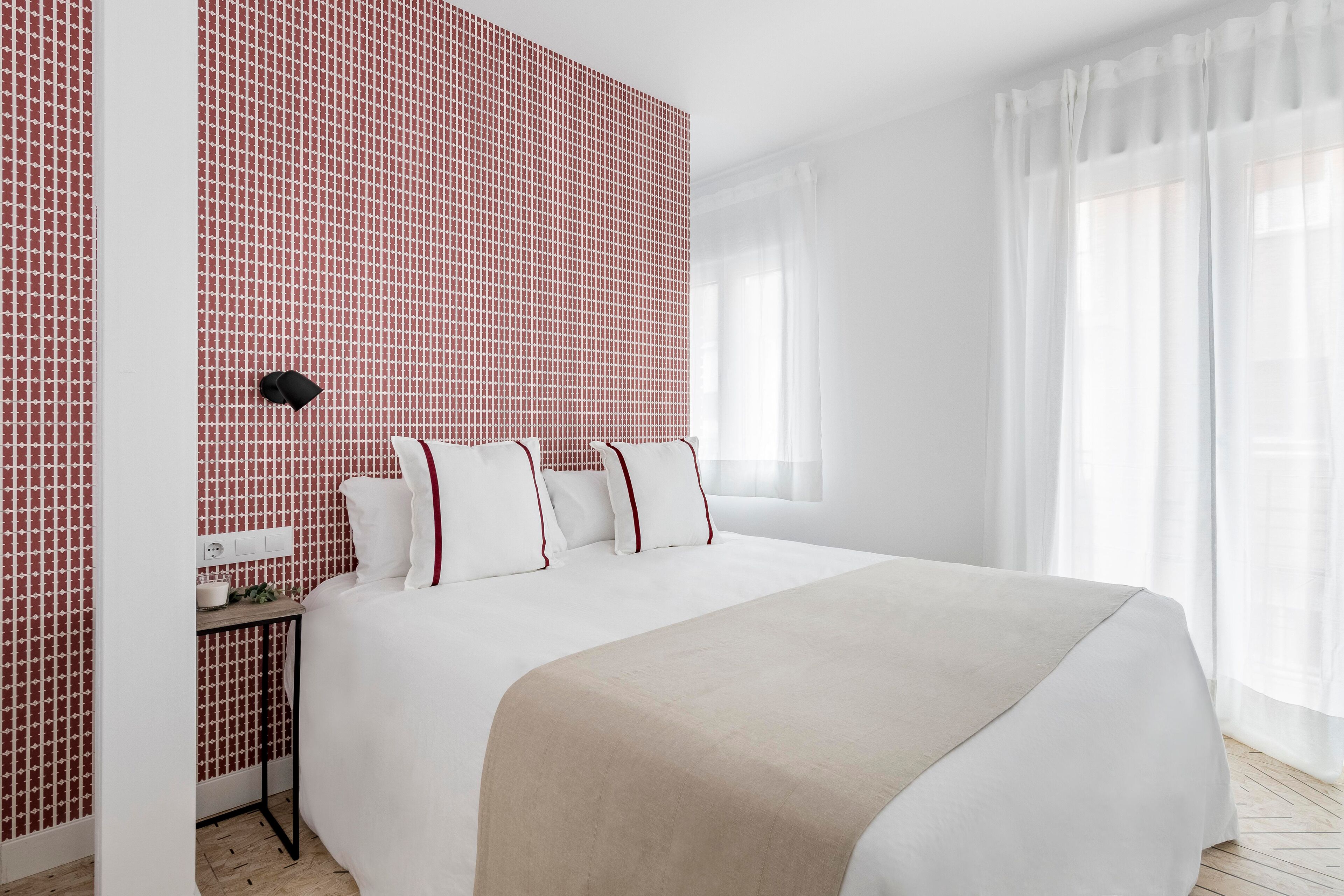 Camera d'albergo ordinata con un letto grande, un comodino e una parete con motivo rosso.