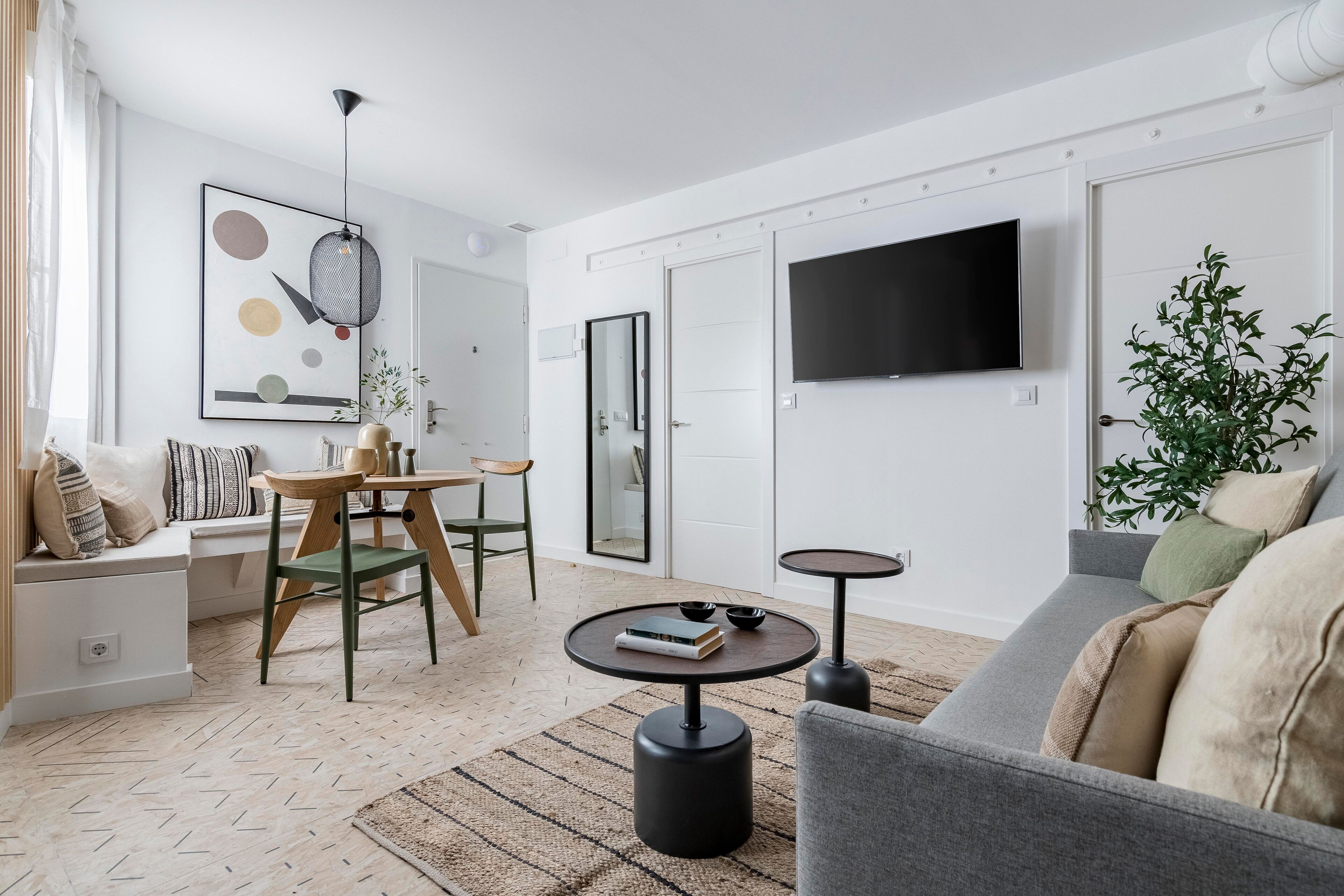 Ein modernes Wohnzimmer mit einer Couch, einem Couchtisch, einem Esstisch mit Stühlen, einem an der Wand befestigten Fernseher und einer Topfpflanze.