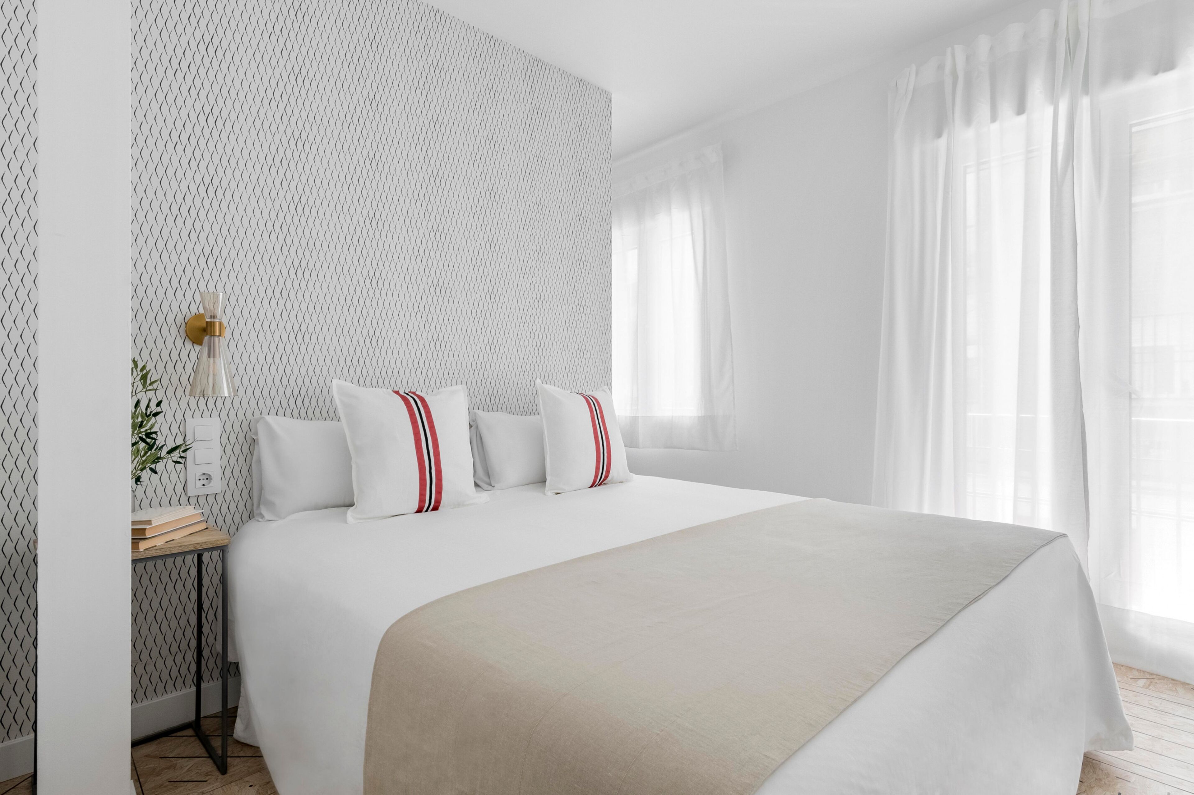 Habitación de hotel impecable con una cama grande, una mesita de noche con lámpara y una ventana con cortinas translúcidas.