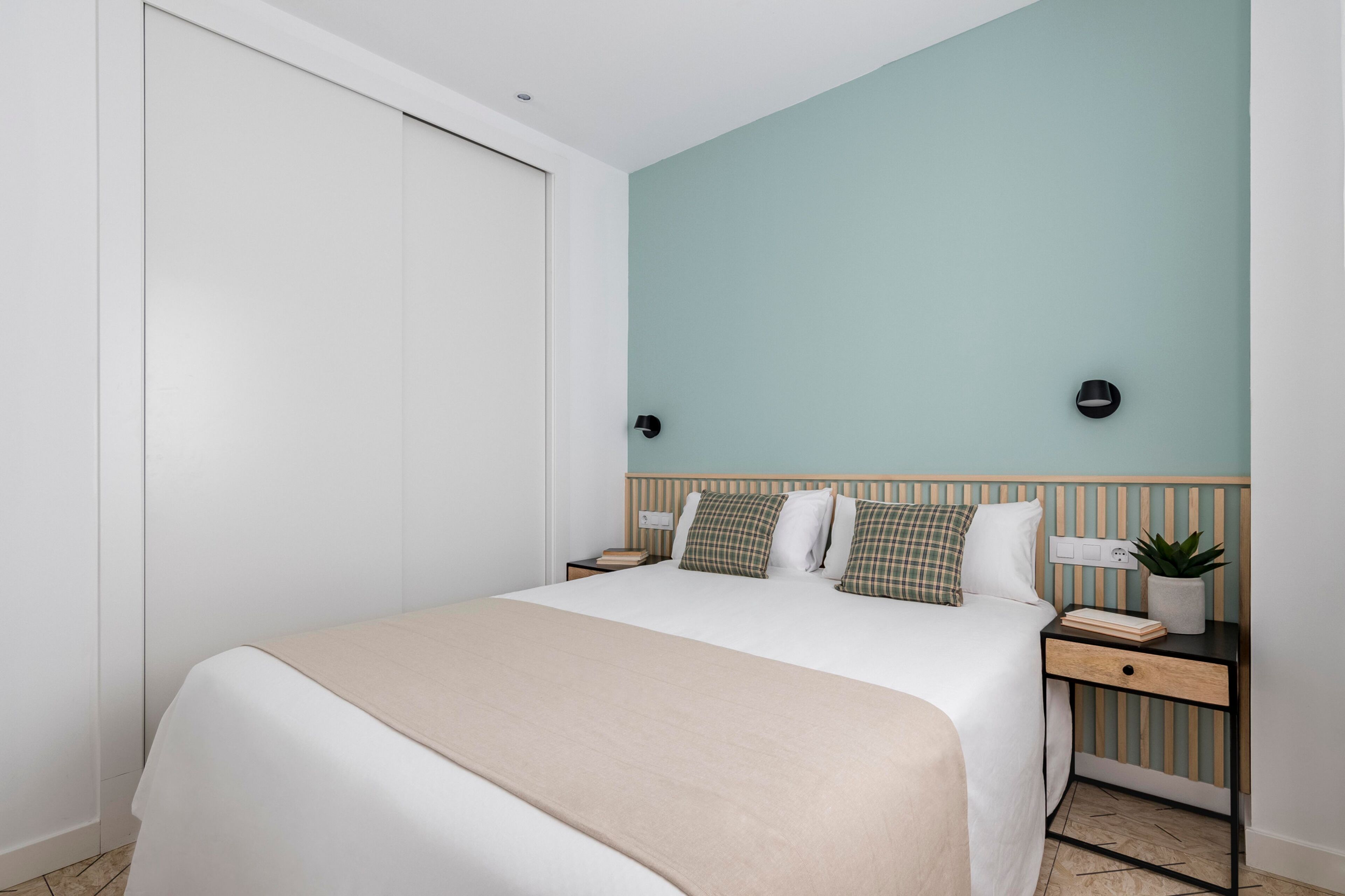 Una habitación de hotel ordenada con cama, mesitas de noche y una lámpara de pared.