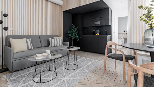 Ein modernes Wohnzimmer mit einem grauen Sofa, einem kleinen runden Tisch und einem Essbereich mit einer Glasvase.