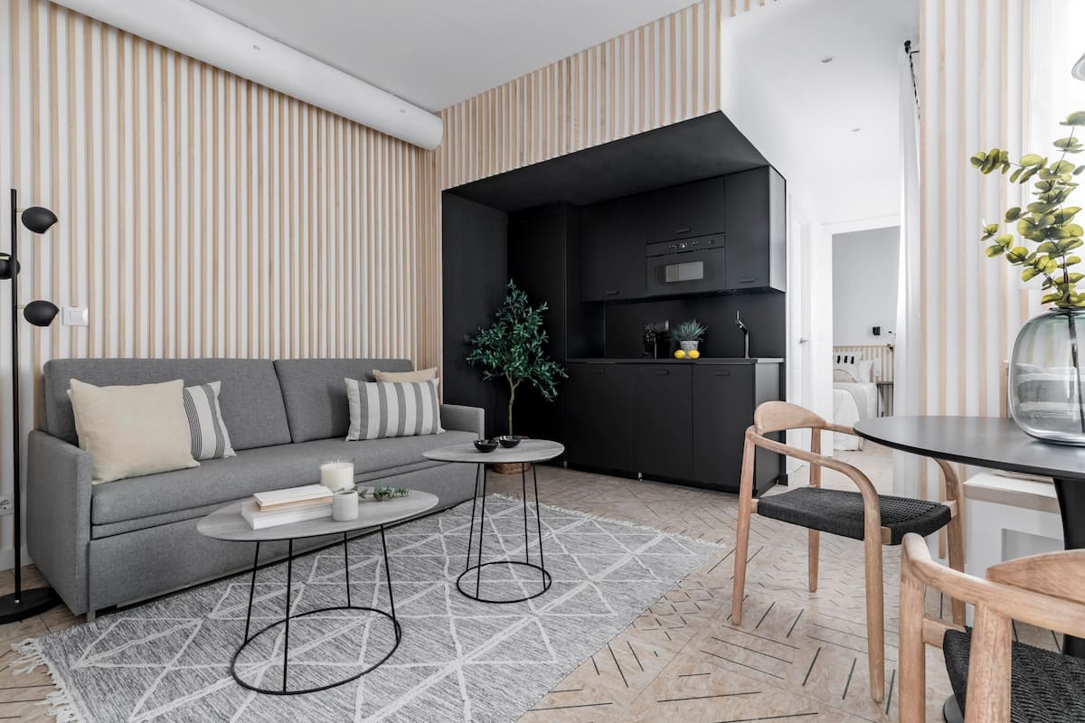 Uma sala de estar moderna com um sofá cinza, uma mesa redonda pequena e uma área de jantar com um vaso de vidro.