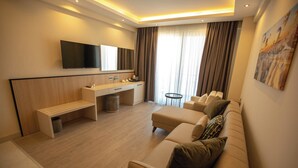 Quarto de hotel moderno com sofá, escrivaninha, televisão e uma janela grande com cortinas.