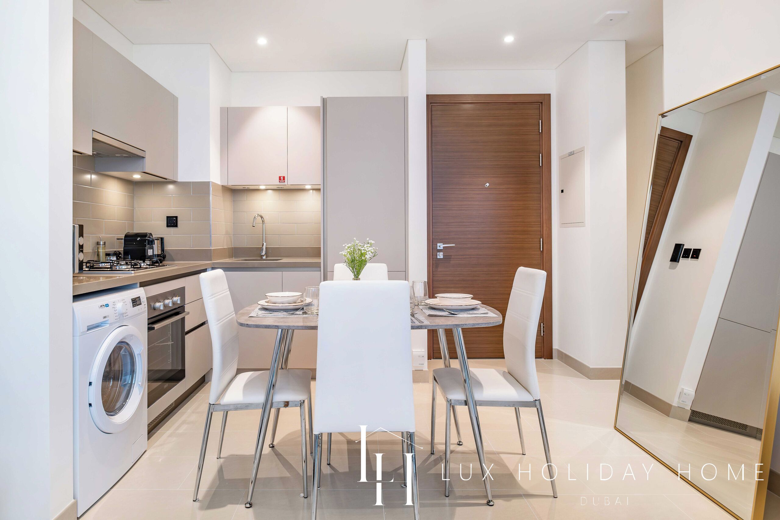 A modern kitchen with a built-in washing machine, a dining area with a table and chairs, and a wooden door.
