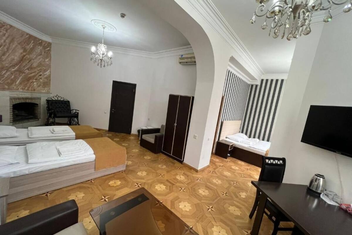 A hotel room with a large bed, a desk, a chair, a TV, and a chandelier.