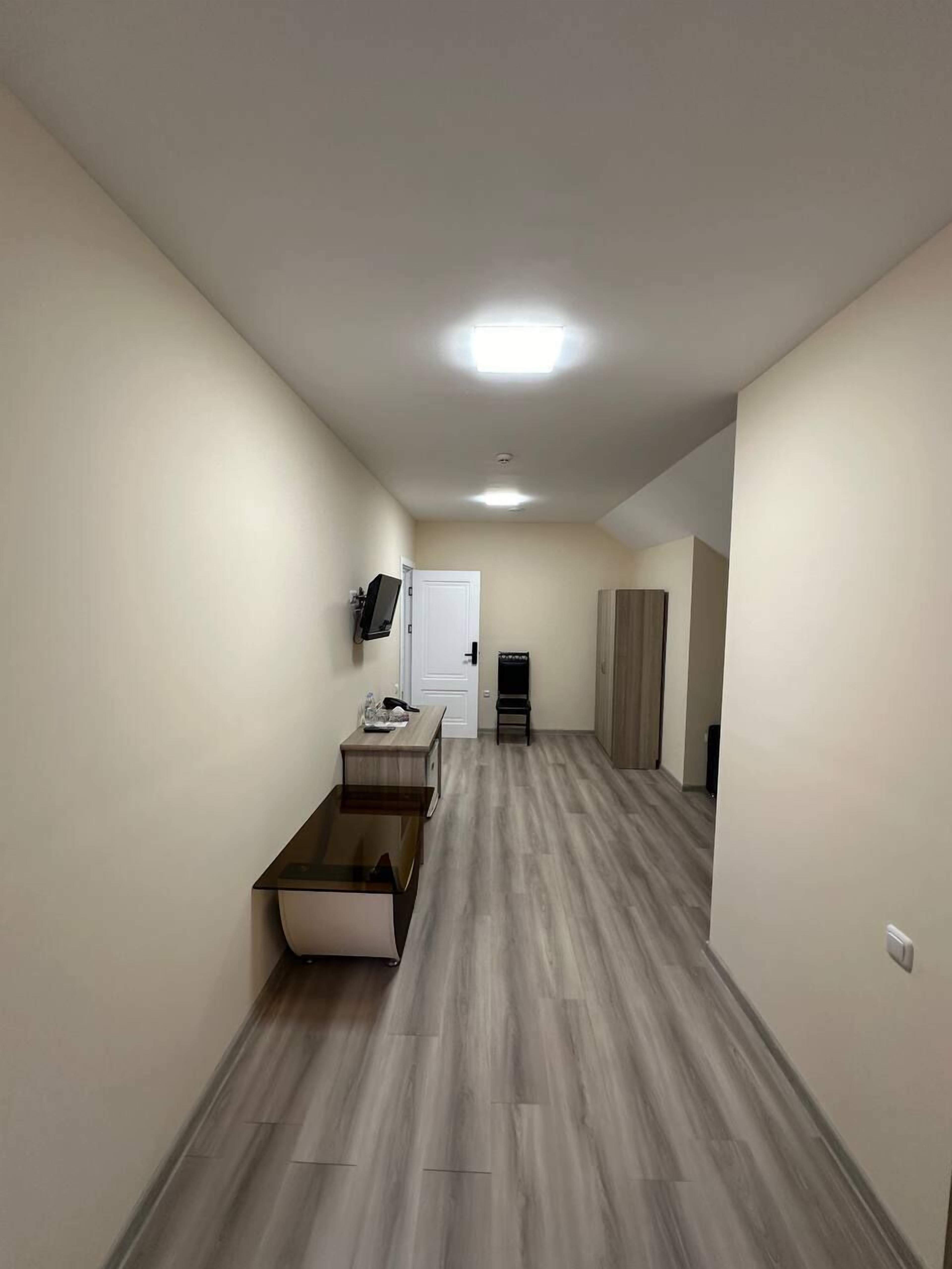 A hallway with a wooden floor, a white door, a small table with a chair, and a wardrobe.