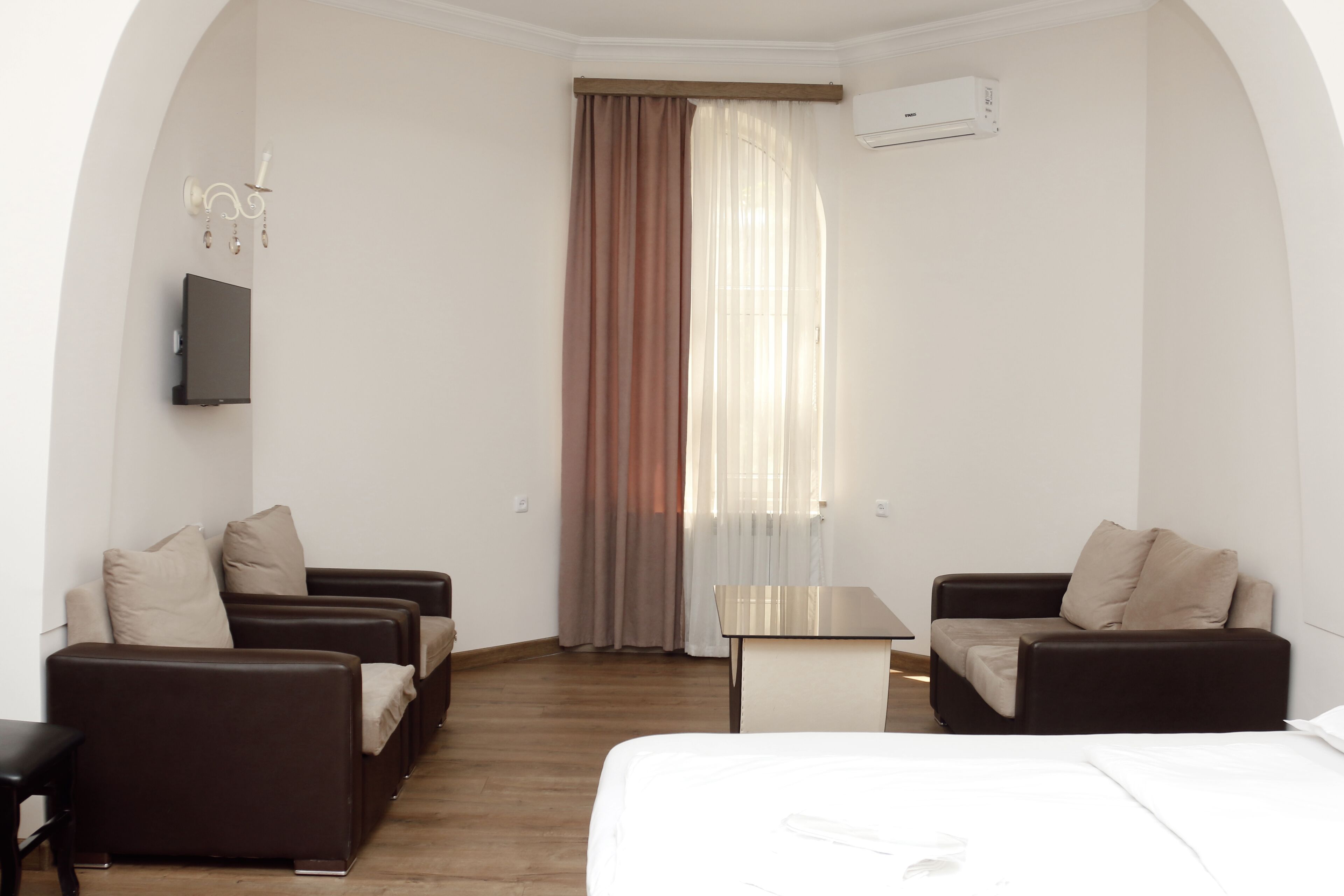 A hotel room with a bed, two sofas, a small table, a TV, and a window with curtains.