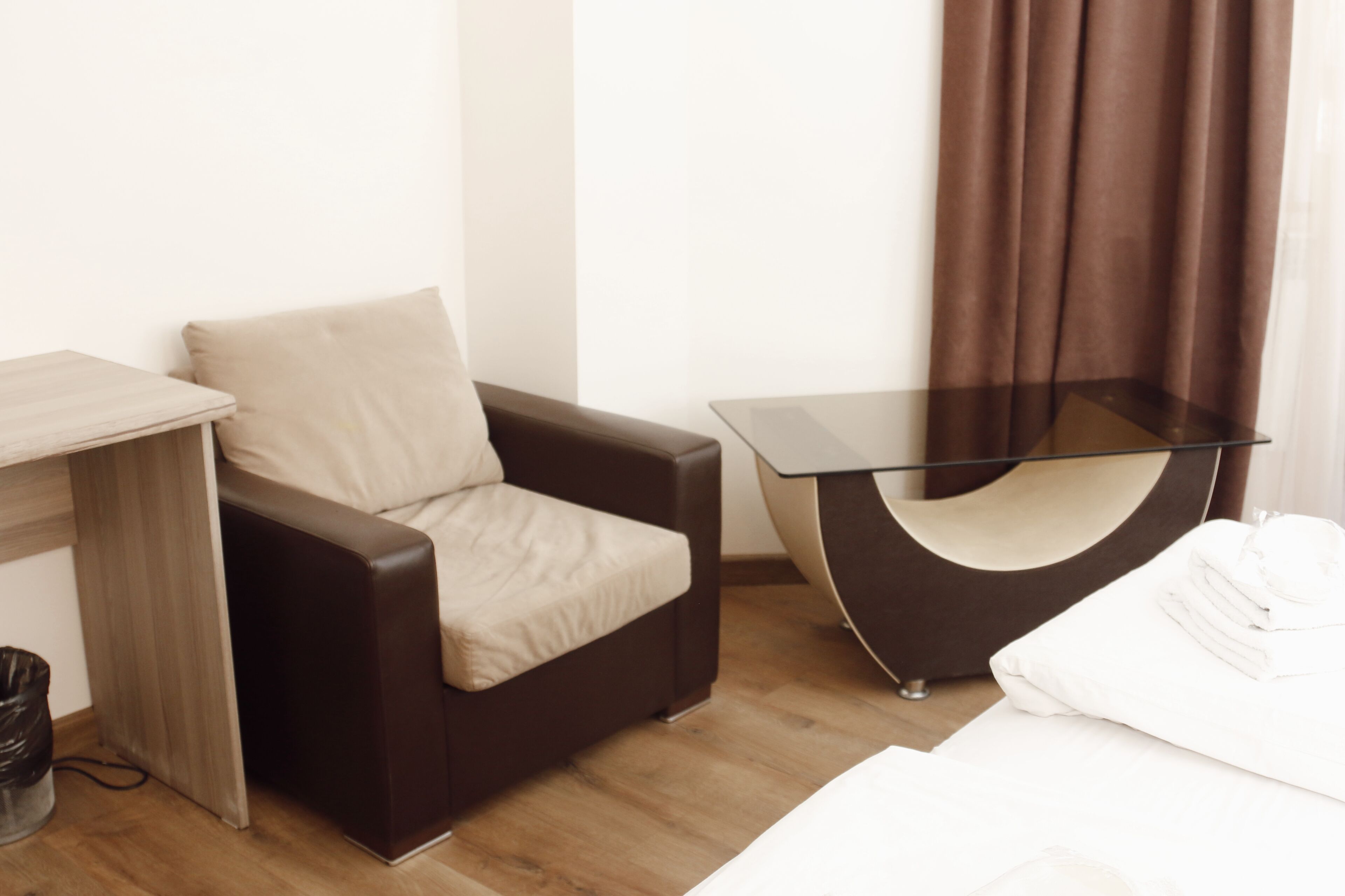 A hotel room with a bed, a brown leather chair, a small table, and a curtain.