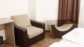 A hotel room with a bed, a brown leather chair, a small table, and a curtain.