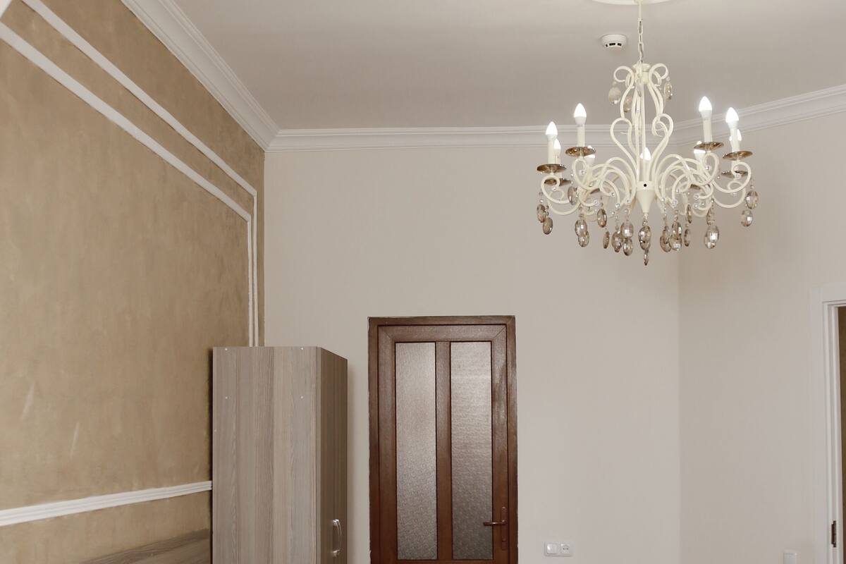 A bedroom with a bed, a wooden wardrobe, a door, and a chandelier.