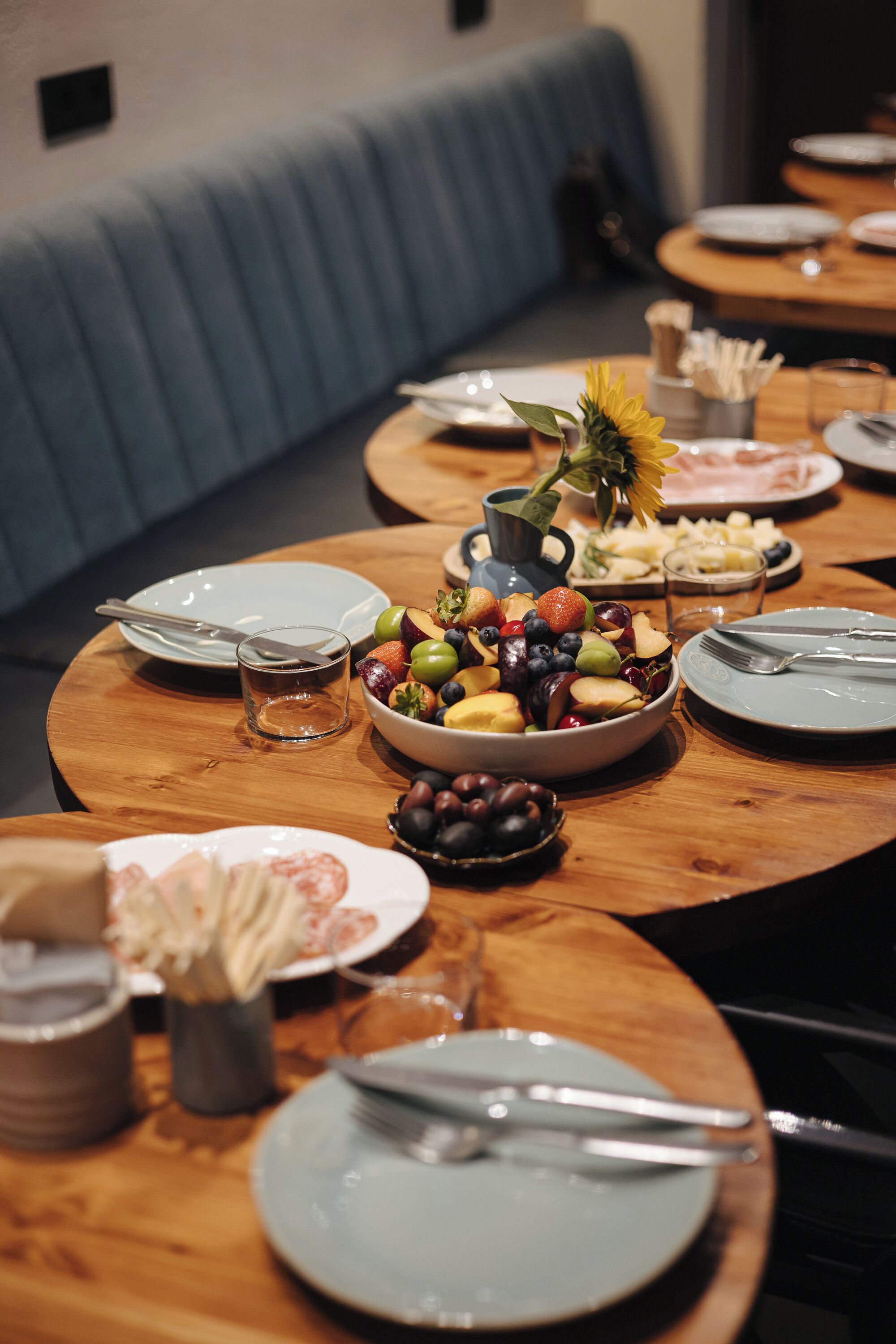 A dining table set with plates, cutlery, and a bowl of fruit.
