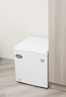 Een kleine witte koelkast met een sticker, geplaatst tegen een houten deur en een lichtgekleurde vloer.