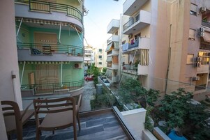 A residential building with balconies, a small outdoor seating area, and a narrow street view.
