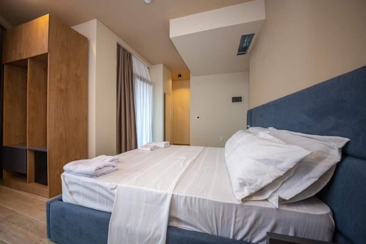 A modern hotel room with a large bed, a wooden wardrobe, and a view of the hallway.