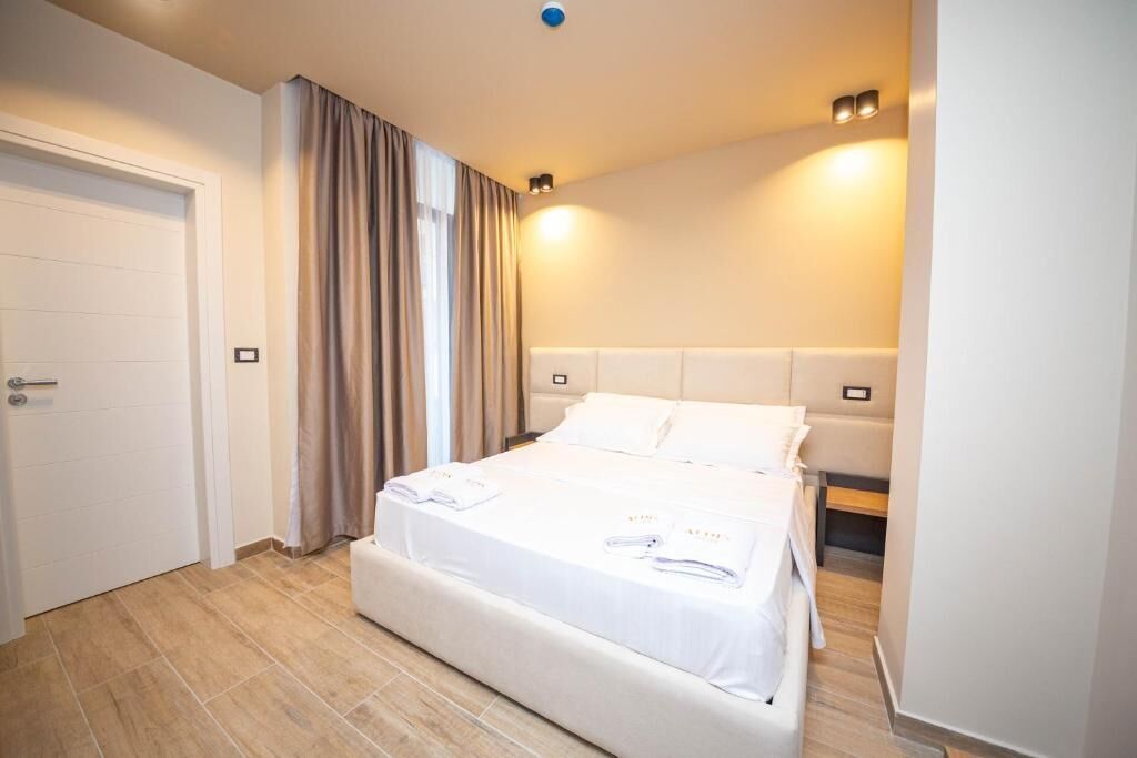 A hotel room with a bed, curtains, a door, and a light fixture.