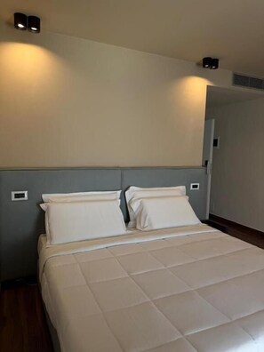 A hotel room with a bed, two wall-mounted lights, and a door.