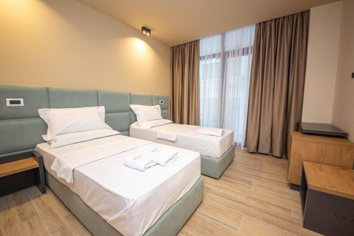 A hotel room with two beds, a desk, and a window with curtains.