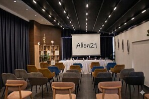 A conference room with a white projection screen displaying 'Alion21,' rows of chairs, and a stage with a podium.