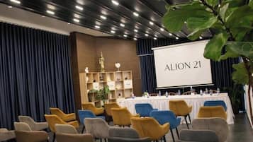Un salón de conferencias con una pantalla de presentación que muestra 'ALION 21', una larga mesa con sillas y una estantería decorativa con objetos.