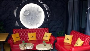 A red sofa with yellow pillows, a round table, and a wall mural of the moon. - Hotel Alion21 (Durrës)