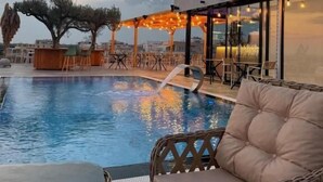 A pool area with seating, a covered seating area, and a building with large windows. - Hotel Alion21 (Durrës)