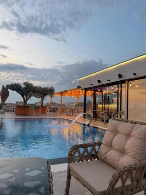 A pool area with seating, a covered seating area, and a building with large windows.