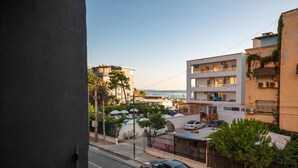 A residential street with cars parked along the side, a building with multiple balconies, and a view of the sea in the background. - Hotel Alion21 (Durrës)
