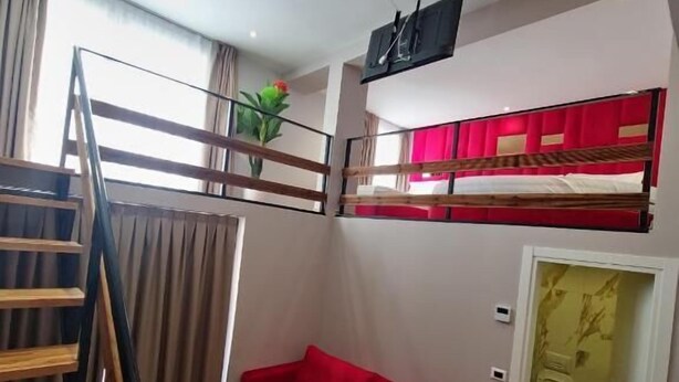 A room with a red sofa, a wooden staircase, a small round table, a TV mounted on the wall, and a door leading to a bathroom. - Hotel Alion21 (Durrës)