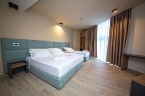 A hotel room with two beds, a small bedside table, a built-in shelf, and a large window with curtains. - Hotel Alion21 (Durrës)