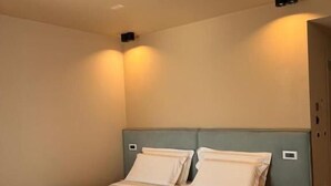A single bed with a headboard, a bedside table, and a wall-mounted light fixture. - Hotel Alion21 (Durrës)