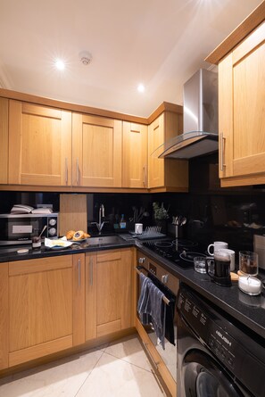 A modern kitchen with wooden cabinets, a stainless steel range hood, a dishwasher, and a microwave.