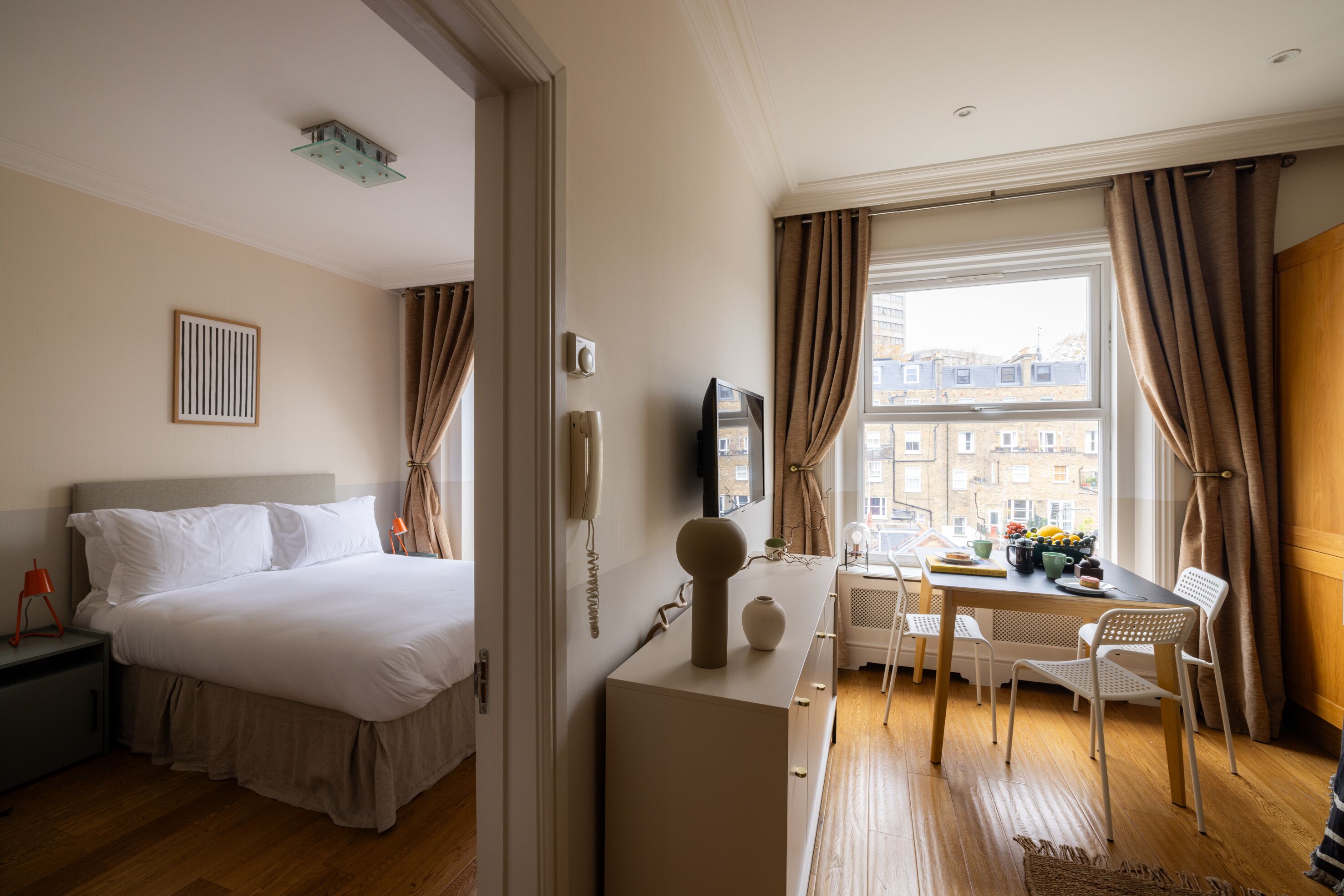 Habitació d'hotel amb un llit, una escriptori amb una cadira, una finestra amb cortines i vista a edificis.