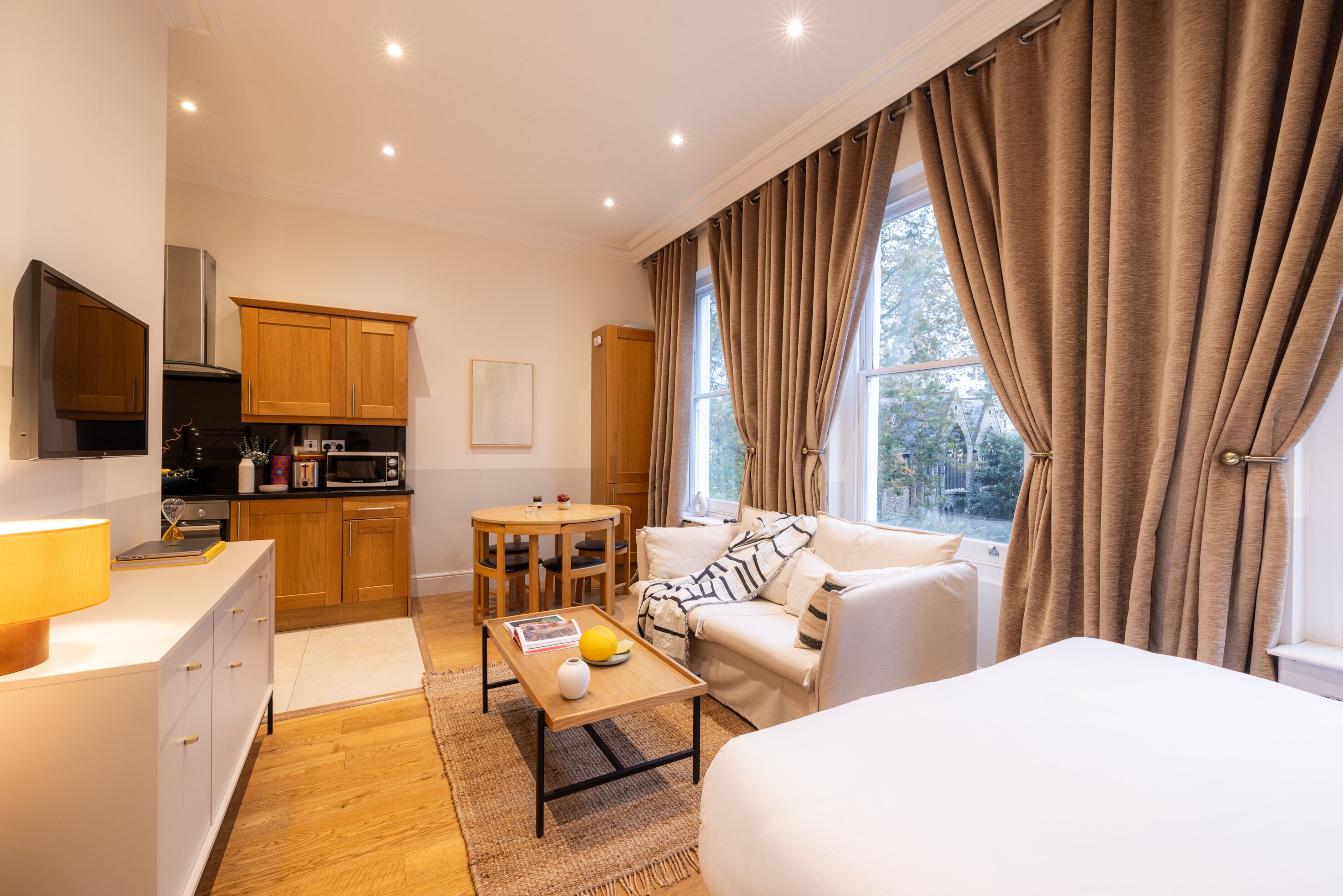 A modern hotel room with a kitchenette, a dining area, a sofa, and a bed.