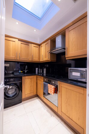 A compact kitchen with wooden cabinets, a built-in oven, a microwave, and a washing machine.